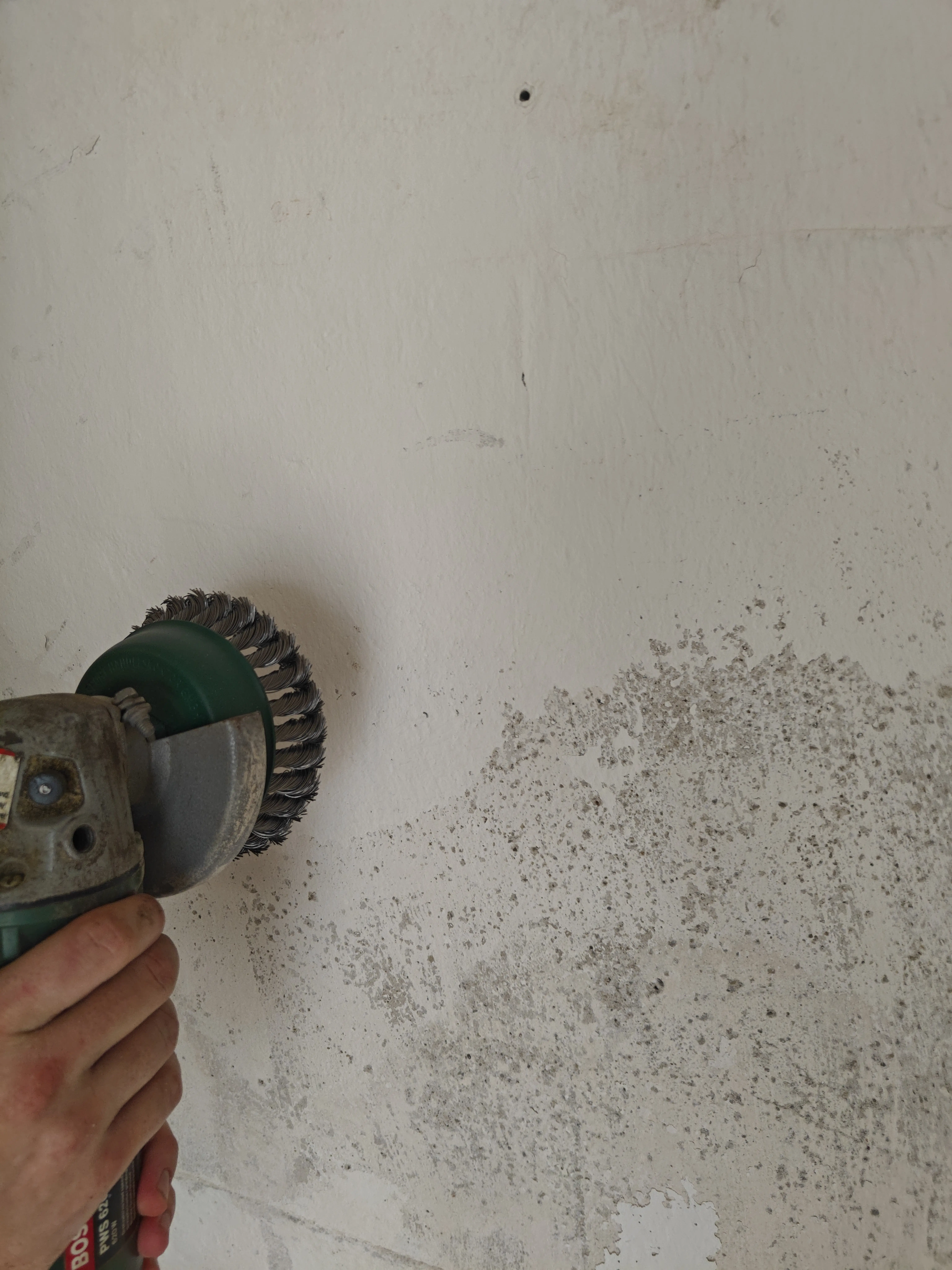 Alter, durchfeuchteter Putz wird mit Spachtel und Hammer von der Kellerwand abgeschlagen